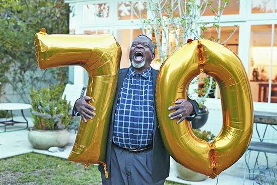 Man with number 70 balloons laughing in backyard